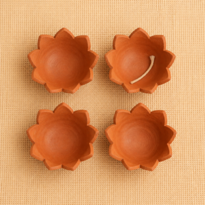 Overhead view of four handcrafted terracotta lotus diyas, with one cotton wick