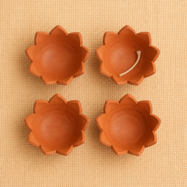 Overhead view of four handcrafted terracotta lotus diyas, with one cotton wick